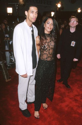 Aaliyah attends the premiere of Romeo Must Die with her brother Rashad Haughton, she is wearing a sheer black and embellished long top over opaque black embellished trousers and sandals