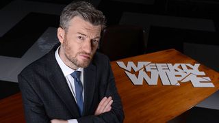 Charlie Brooker with his arms folded next to the Weekly Wipe logo