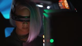 Still from the Star Wars TV show Skeleton Crew. Close up of KB (she has a white asymmetrical bob and has a visor over her eyes) as she works at navigation data on a screen in front of her.