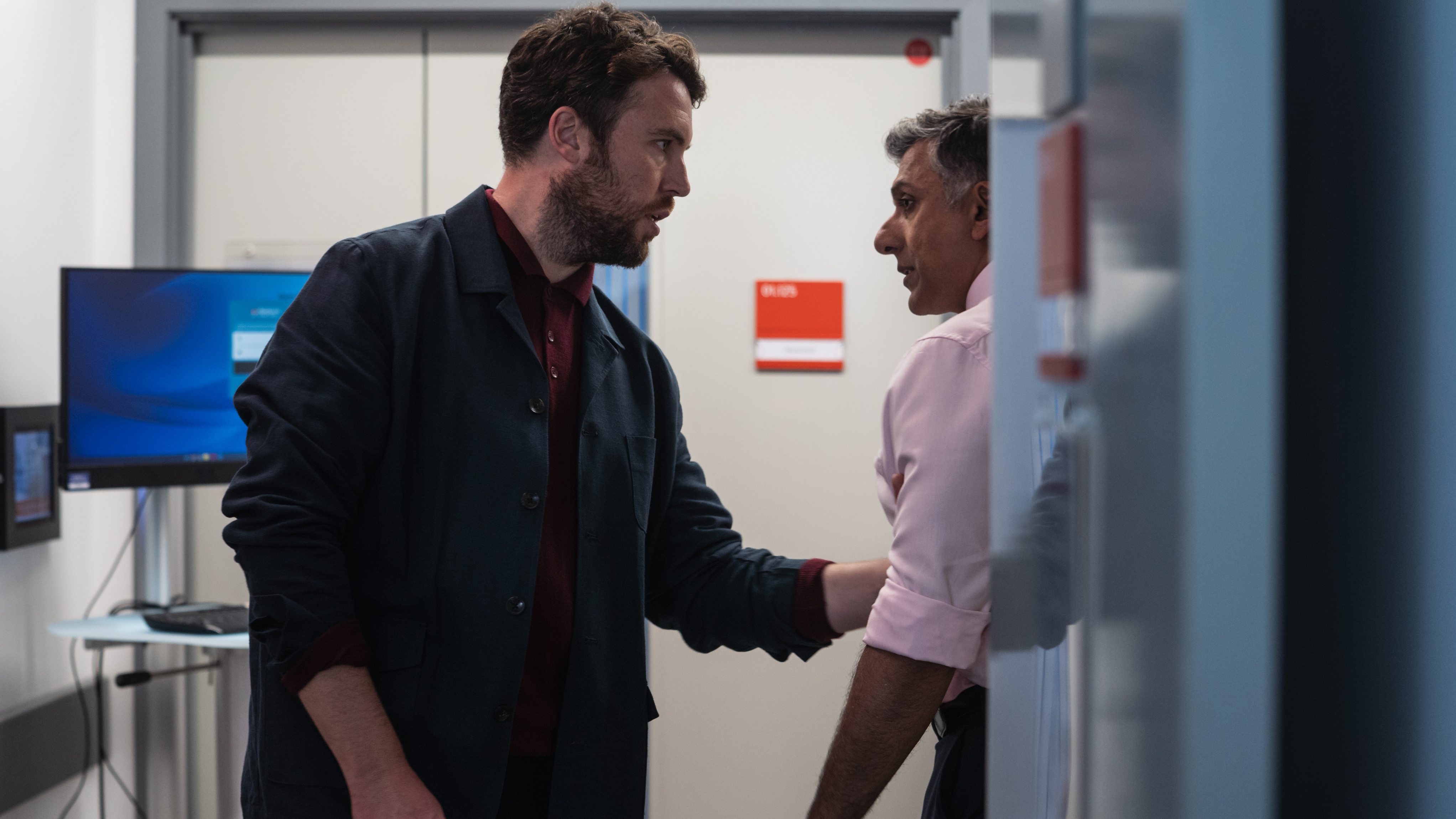 James looking wound up as he grabs Arun's arm in a hospital corridor