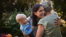 A woman hugs her older mother while holding her baby