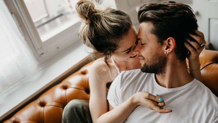 A young woman and man cuddle on a couch.