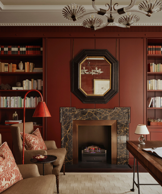 Living space ith dark red walls and fireplace and armchairs and floor lamp and rug