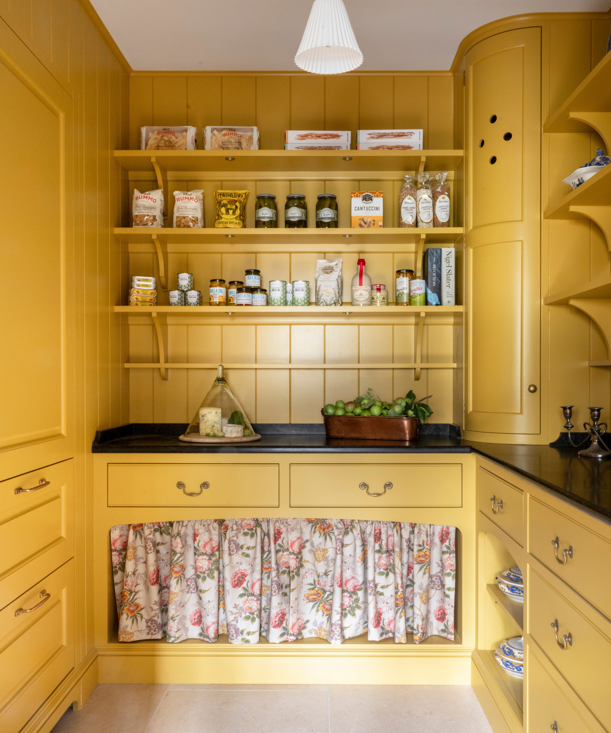A bright yellow pantry with black countertops and a floral cabinet skirt