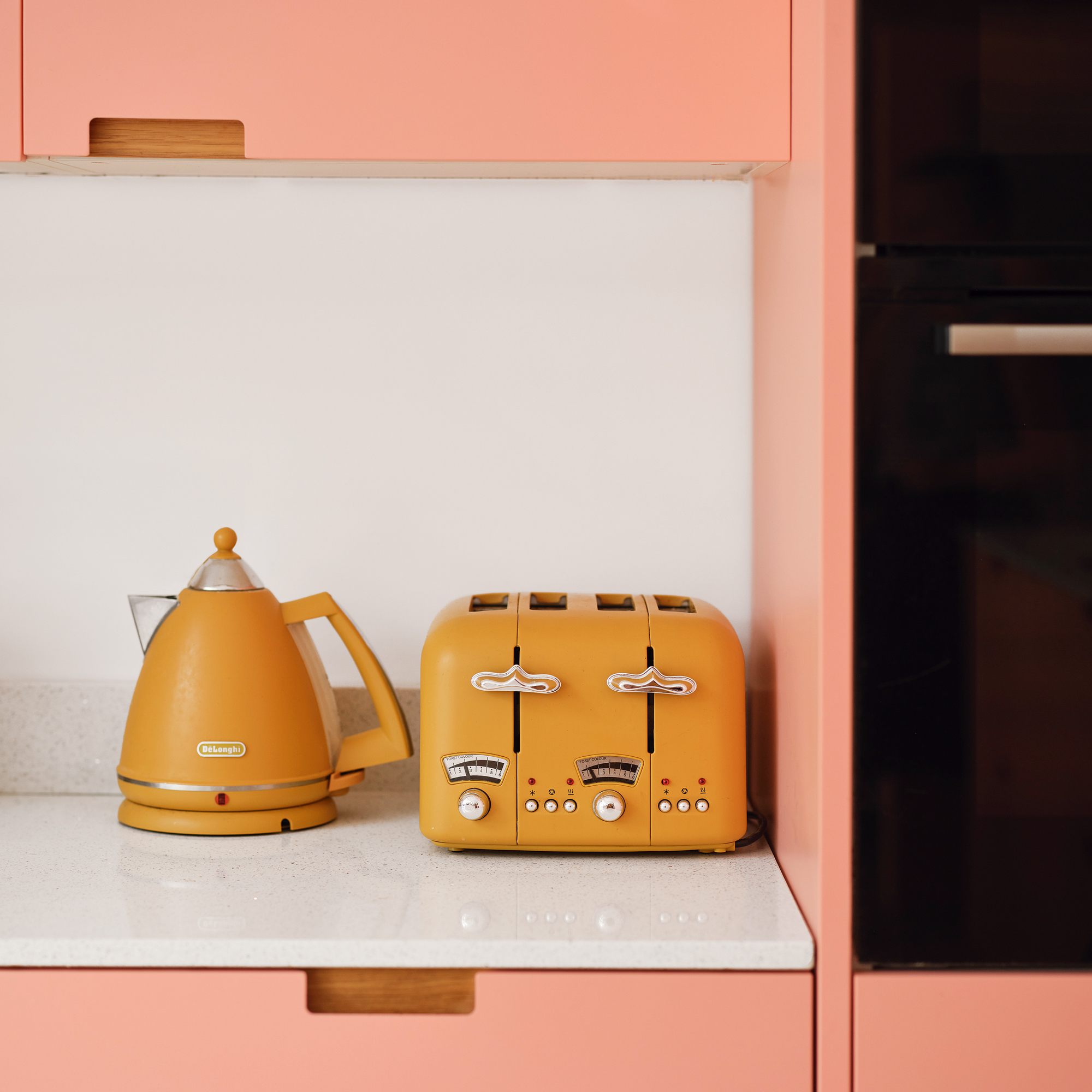 pink kitchen cabinets with a white countertop and matching yellow De'Longhi kettle and toaster set