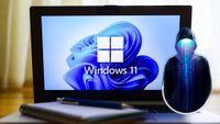 Windows 11 displayed on a laptop, keyboard and pen resting on the keyboard. Overlaid on top of this image is a photo illustration of a hacker, code pouring out from beneath the brim of their hood.
