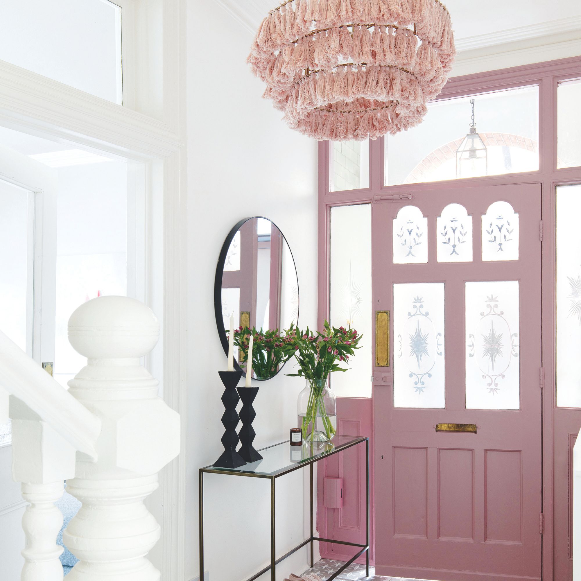 A white hallway with pink accent door and pink textured chandelier light