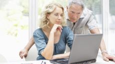 An older couple look at a laptop together in their kitchen.