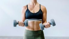Torso of a fit woman hodling dumbbells in each hand
