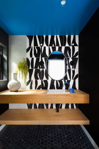 Black bathroom with blue ceiling and black and white patterned wall tiles