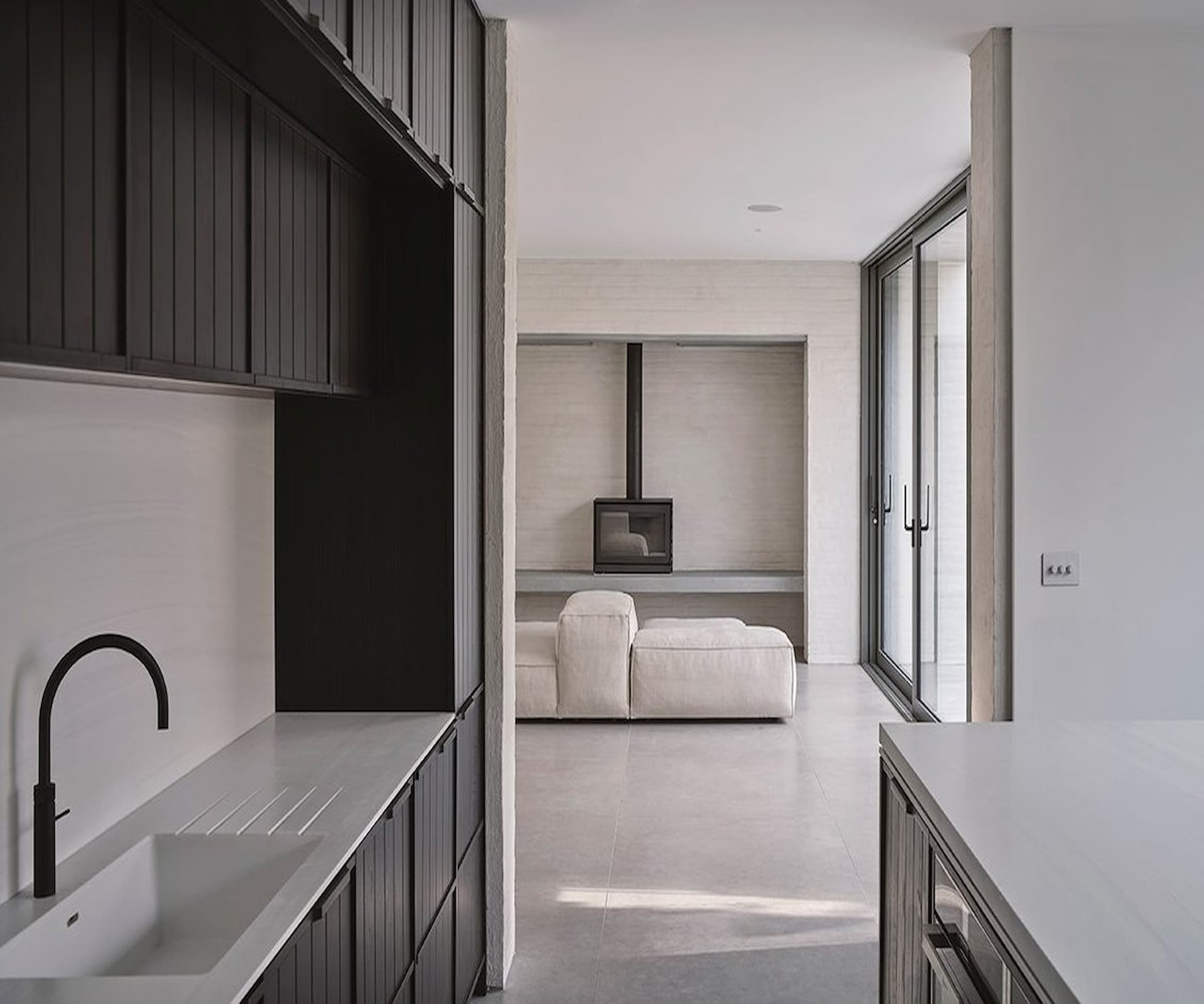 A white kitchen leading onto a living room with a black log burner