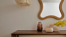 An entryway with a wood table, a hanging mirror, pendant lighting and a pair of bowls