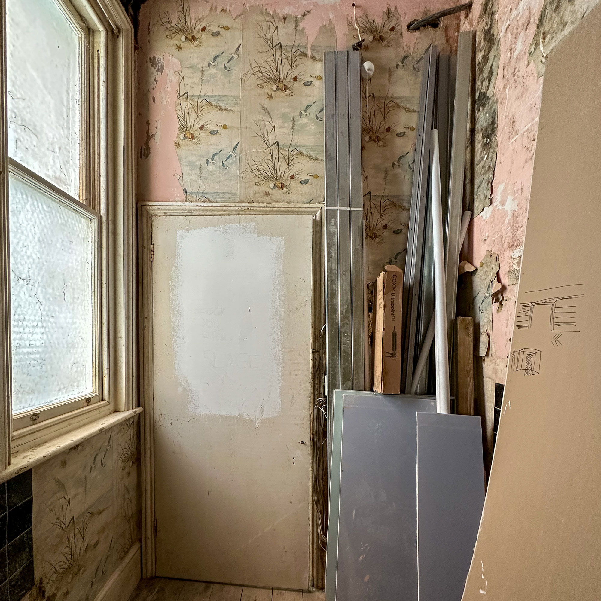Room mid-renovation with piles of building materials and floral patterned wallpaper semi-stripped from walls