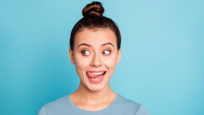 woman with olaplex bun sticking out her tongue, blue background
