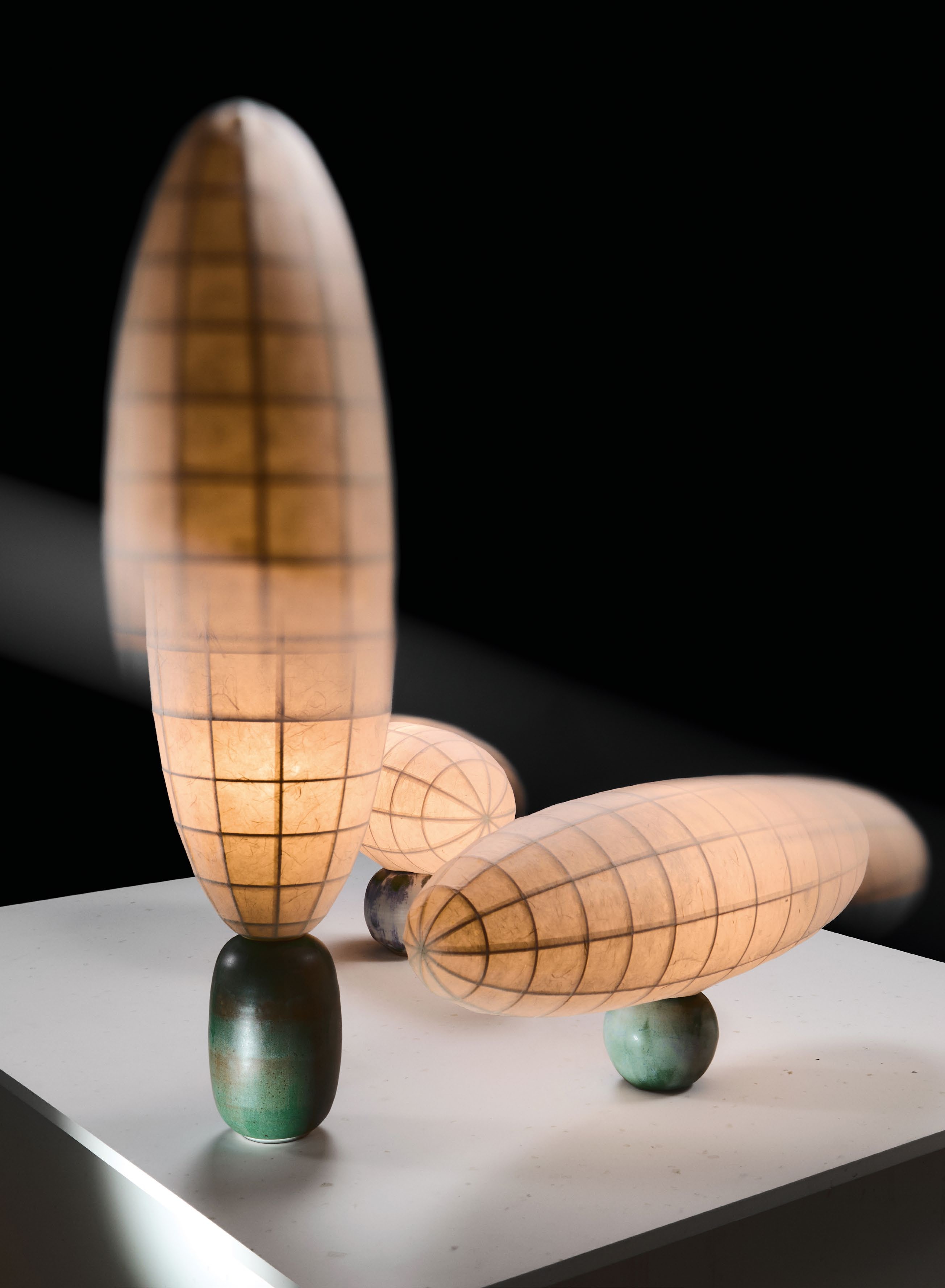 A collection of contemporary lamps designed by Steffany Tran, featuring ceramic bases and lampshades made of traditional Vietnamese dó paper, showcased on a minimalist display.