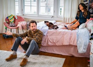 a man (charlie day) sits on the floor and leans against a bed as a woman (gina rodriguez, right) sits atop the bed against the pillows, in the 'prime video' rom-com 'i want you back'