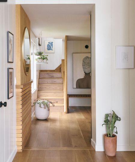 Neutral entryway with warm wooden flooring, stairs and wall panelling, white walls, planters on floor, artwork on walls