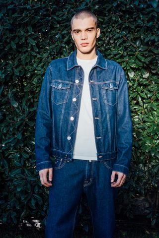 Man in Jacob Cohën jean jacket, white T-shirt and jeans against leafy wall
