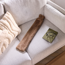 Aldi long hot water bottle in brown on a white sofa.