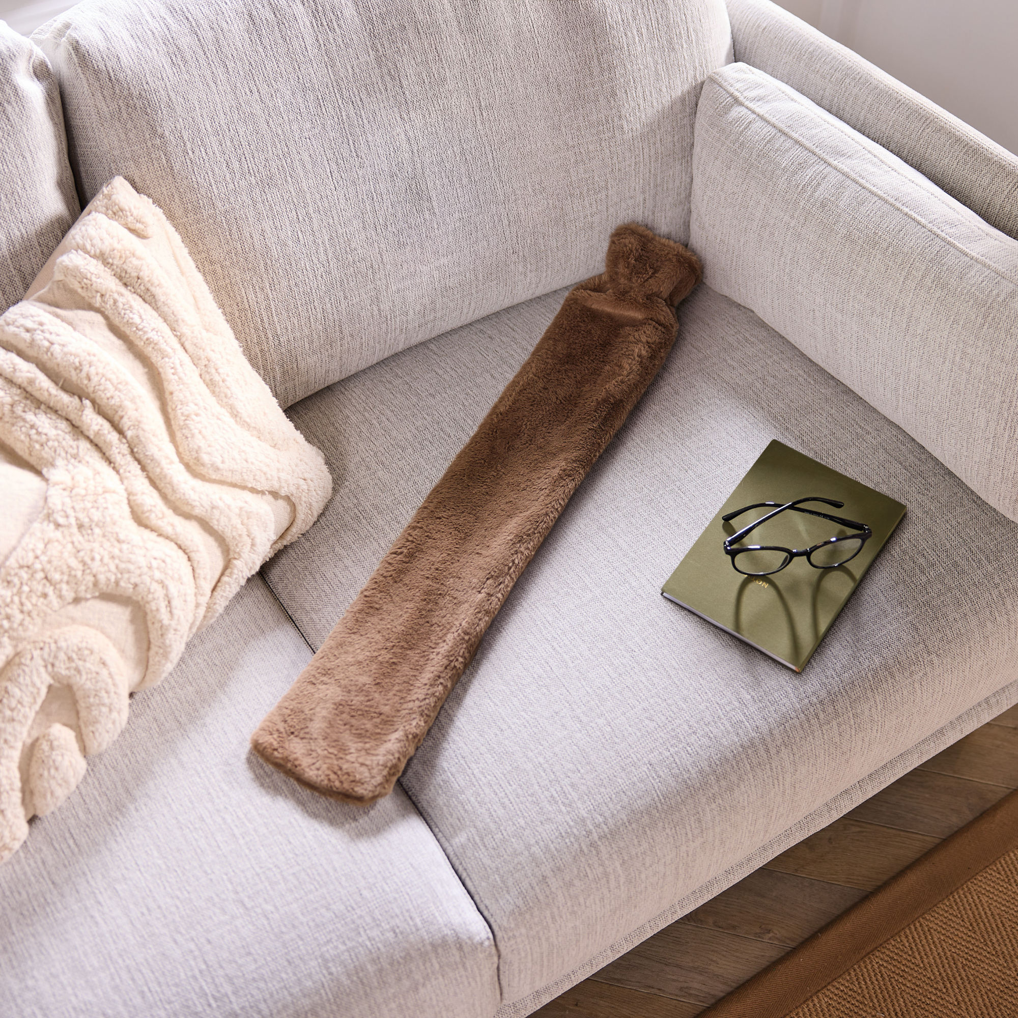 Aldi long hot water bottle in brown on a white sofa.
