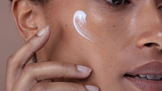 A close-up shot of a woman with a thick cream on her cheekbone, to show what is barrier cream