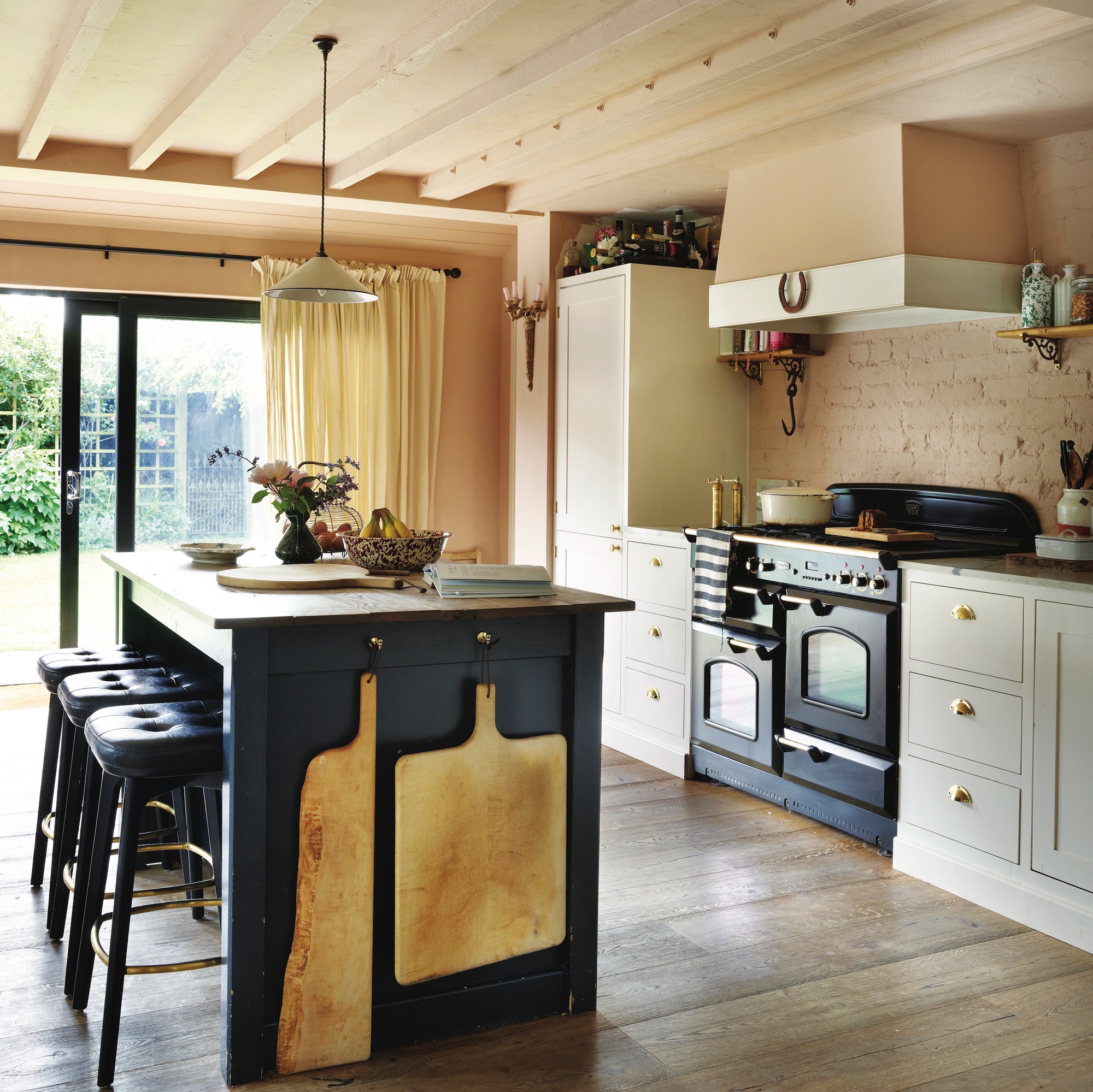 cottage kitchen with dark painted island with bar stools and large chopping boards hung on side