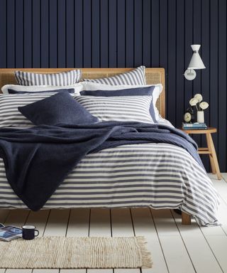 A white and blue bedroom with navy blue shiplap wall, white floorboards and wooden bed with blue and white striped bedding