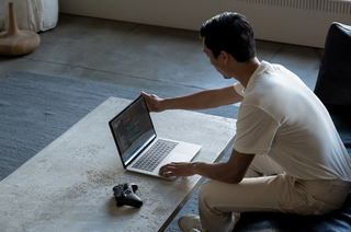 A man sitting in front of an open Microsoft Surface Laptop Studio on a low table