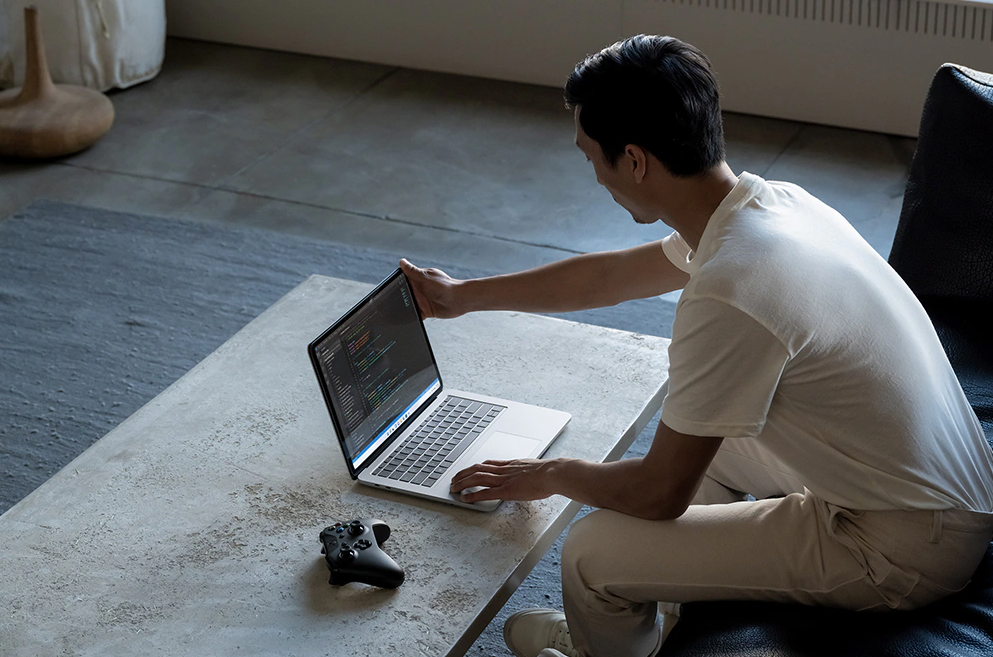 A man sitting in front of an open Microsoft Surface Laptop Studio on a low table