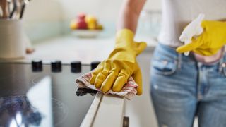 gloved hands cleaning kitchen surfaces to show how often you should clean your house