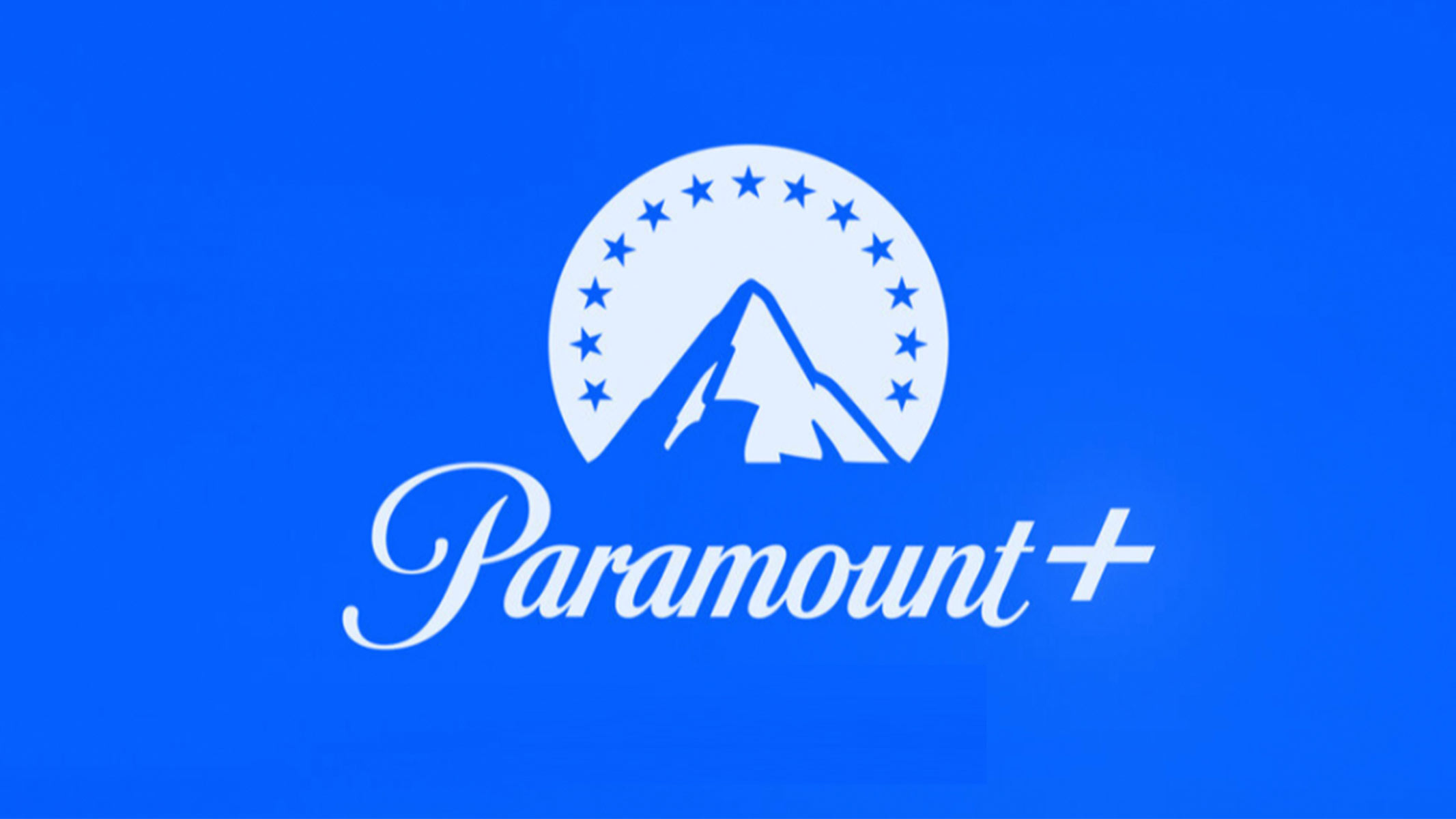 "Paramount +" written in cursive writing with a white mountain and circle behind it on a blue background with blue stars surrounding the mountain