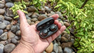 Sony WH-1000XM4 headphones inside open charging case placed in palm of reviewer's hand