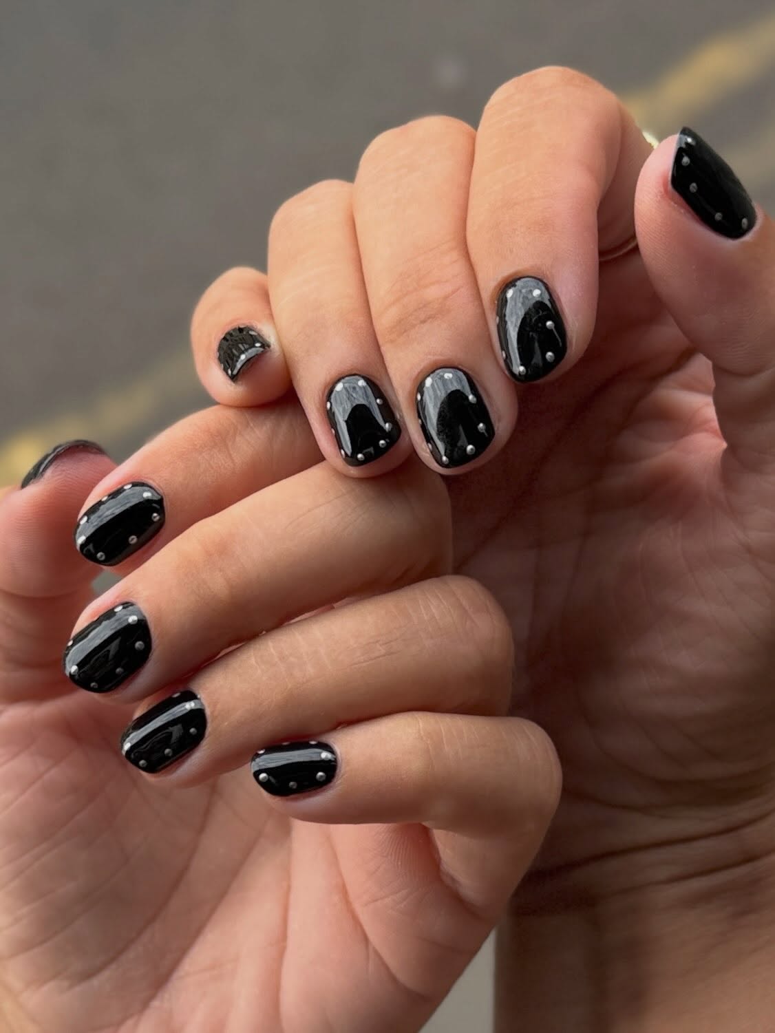 Glossy black nails outlined with a polka dot silver metallic border