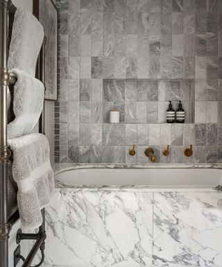 A modern bathroom with marble tiling, a marble bath and gray towels