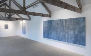 Large paintings in a blue wash with writing on them are hung in the gallery.