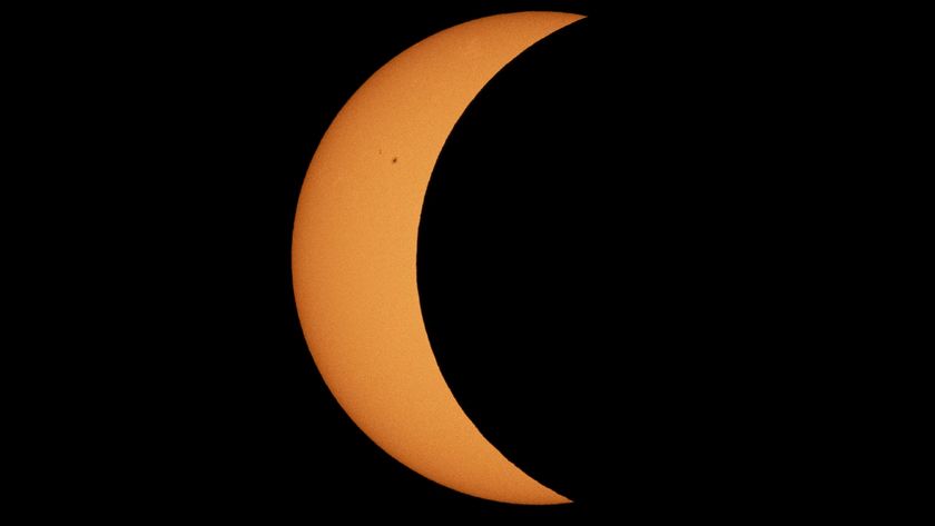 A photo of the sun captured during a partial solar eclipse. The silhouette of the moon covers the majority of the sun, transforming it into a crescent, or sickle shape.
