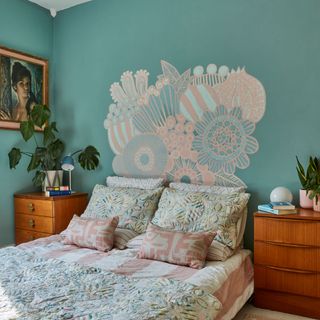 Blue bedroom with pink painted design over bedhead and wooden bedside drawers