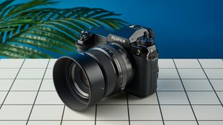 The Fujifilm GFX100S II on a white surface with a blue wall in the background