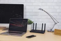 TP-Link Archer AX3000 on a wooden desk with a laptop and smartphone