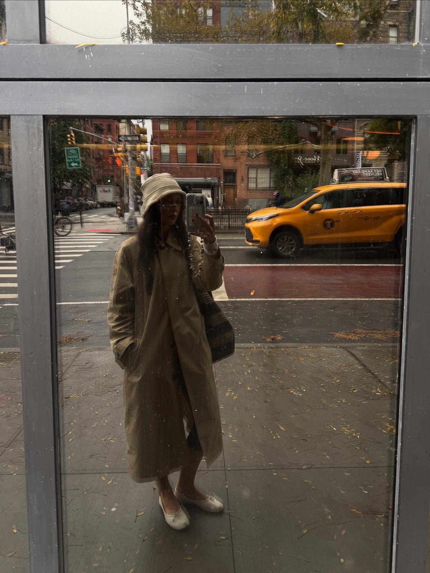 Influencer @makenna_alyse takes a mirror selfie on the street in New York wearing a tench coat, white ballet flats and a knitted bucket hat.