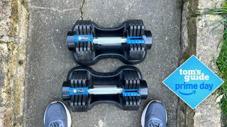 LifePro PowerFlow Plus adjustable dumbbells next to someone's feet on a garden path