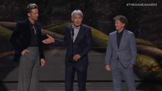 Harrison Ford standing on stage between Troy Baker and Todd Howard while pointing to Howard