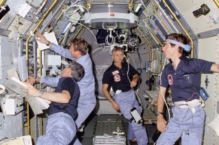 STS-9 crew members working on science experiments inside the European Spacelab 1 module, November 1983.