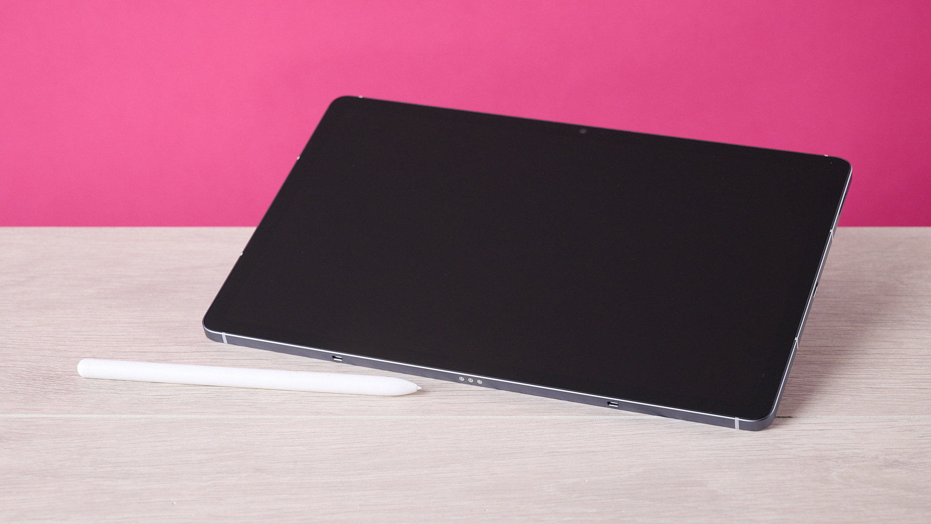 The Samsung Galaxy Tab S10 FE sat at an angle on a table behind the S Pen and in front of a pink background.