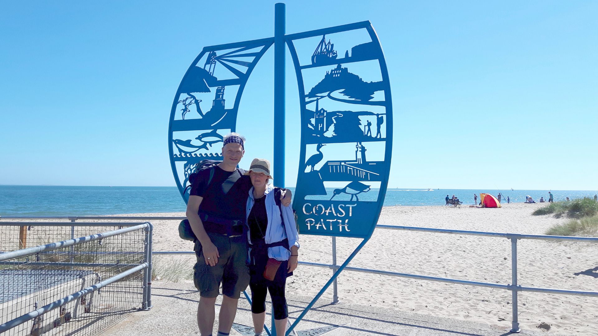 Raynor Winn and Moth standing at the end of the South West Coastal path in the sunshine