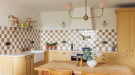 An L-shaped kitchen with pale yellow cabinets, a large wooden table, and a checkerboard backsplash