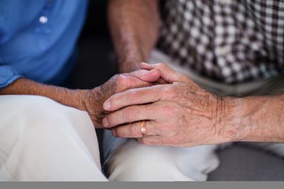 An elderly couple holds hands.