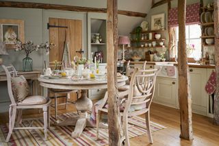 vintage kitchen with round table and four chairs in center. Open plan space is seperated by rustic beams and to the back of the picture is a white kitchen