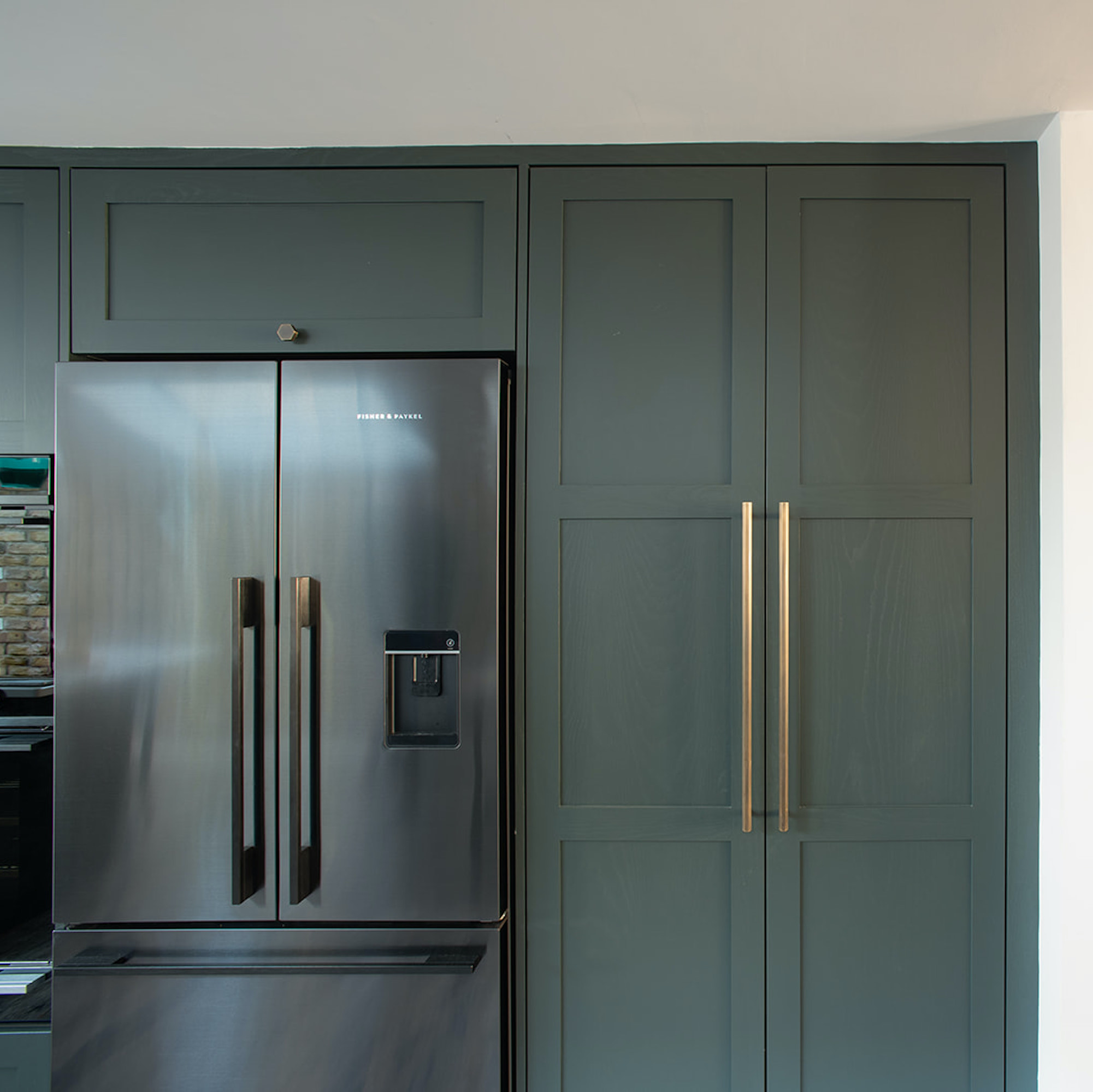 green-grey shaker kitchen with brass handles and fridge freezer
