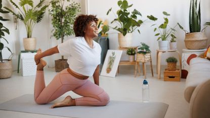 Woman stretching on workout app at home, smiling and surrounded by plants, using one of the best Pilates apps